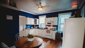 Une cuisine avec des meubles blancs, une table à manger en bois et un ventilateur de plafond.