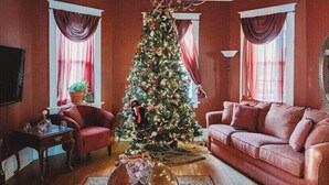 Un salon décoré d’un sapin de Noël, avec des rideaux rouges, un canapé rouge et un lustre.