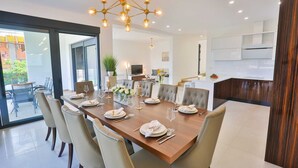 Un espace repas moderne avec une longue table en bois, dressée pour six personnes, entourée de chaises à revêtement beige.