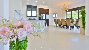 Une cuisine moderne avec des meubles blancs, un coin repas agrémenté d’un lustre, et une grande fenêtre donnant sur un paysage verdoyant.