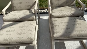 Dos sillones con estampado de palmera, ubicados en un patio de concreto con baranda metálica y una planta en maceta al fondo.