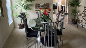 Un comedor con una mesa de vidrio y sillas de metal, rodeado de plantas en macetas y obras de arte en las paredes.