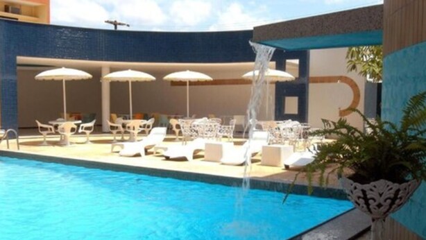 A swimming pool with lounge chairs and umbrellas, surrounded by a building with a blue exterior. - Hotel Praia Ponta D'areia (São Luís)