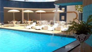 Una piscina al aire libre, sombrillas, sillones reclinables de piscina