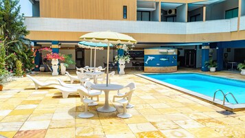 Un área de piscina con sillones reclinables, una mesa y un bar junto a la piscina.