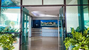 A modern hotel lobby with a glass entrance, a staircase, and a mural of a cityscape. - Hotel Praia Ponta D'areia (São Luís)