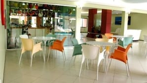 A spacious indoor area with multiple tables and chairs, a glass partition with various items, and a bar area. - Hotel Praia Ponta D'areia (São Luís)
