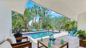 Un área junto a la piscina con una mesa de madera, sillas azules y un sofá blanco.