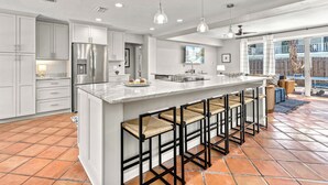 Una cocina amplia con armarios blancos, un refrigerador de acero inoxidable, una isla grande con taburetes de bar e iluminación colgante.