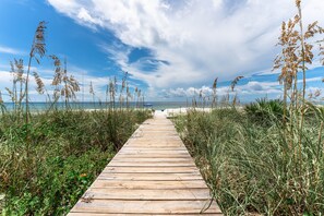 A wooden boardwalk leading to a beach with tall grasses and a clear sky.