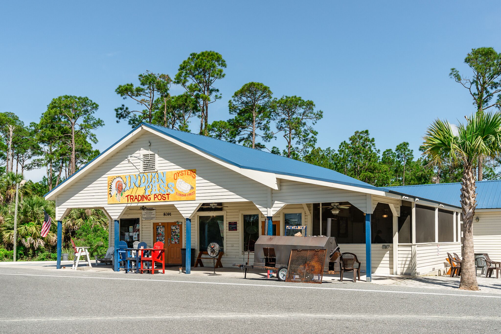 A small, single-story building with a blue roof and a sign that reads "Indian Oysters Trading Post."