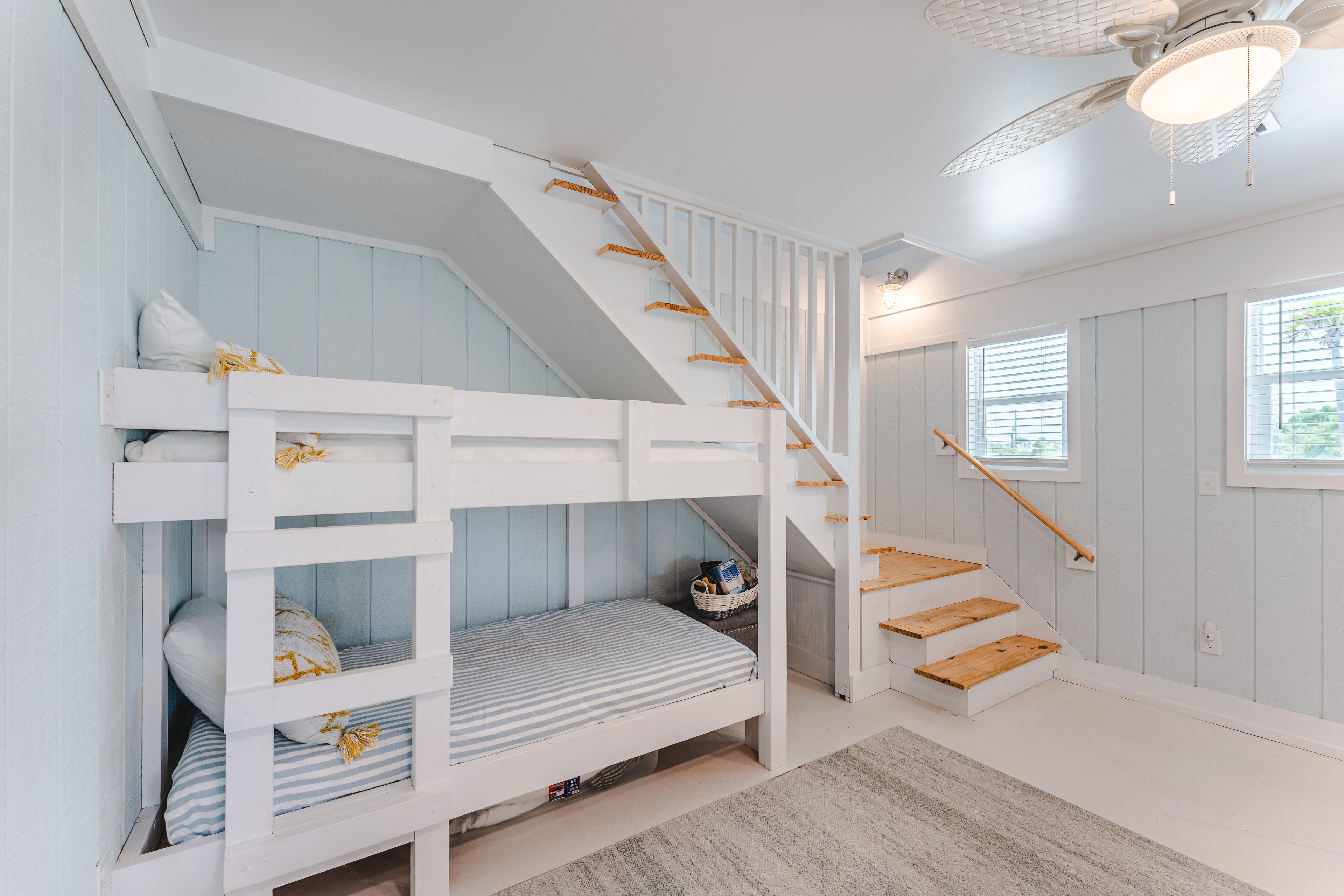 Ein Zimmer mit Etagenbett, Treppe und Deckenventilator.
