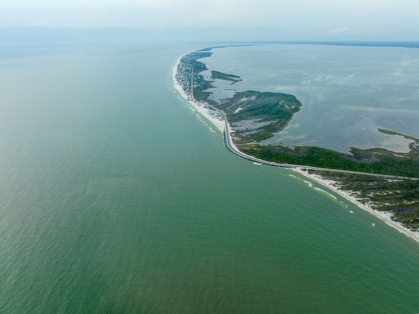 An aerial view of a coastal area with a long stretch of beach and a road curving along the coastline. - Rare find! Discounted 2024 Rates, Cape San Blas!Contact host for details! (Port St. Joe)