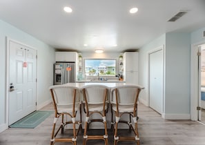 Una cocina moderna con una isla central, muebles blancos y vistas al vecindario.