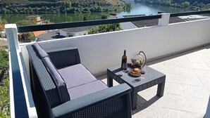 A terrace with a view of a river and hills, featuring outdoor seating and a table with a bottle and glass. - Alojamento 2 Dos Santos (Pinhão)