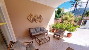 A covered outdoor seating area with wicker furniture, a glass coffee table, and potted plants.