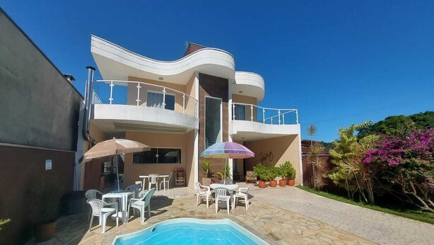 A modern two-story building with a swimming pool, outdoor seating, and potted plants.