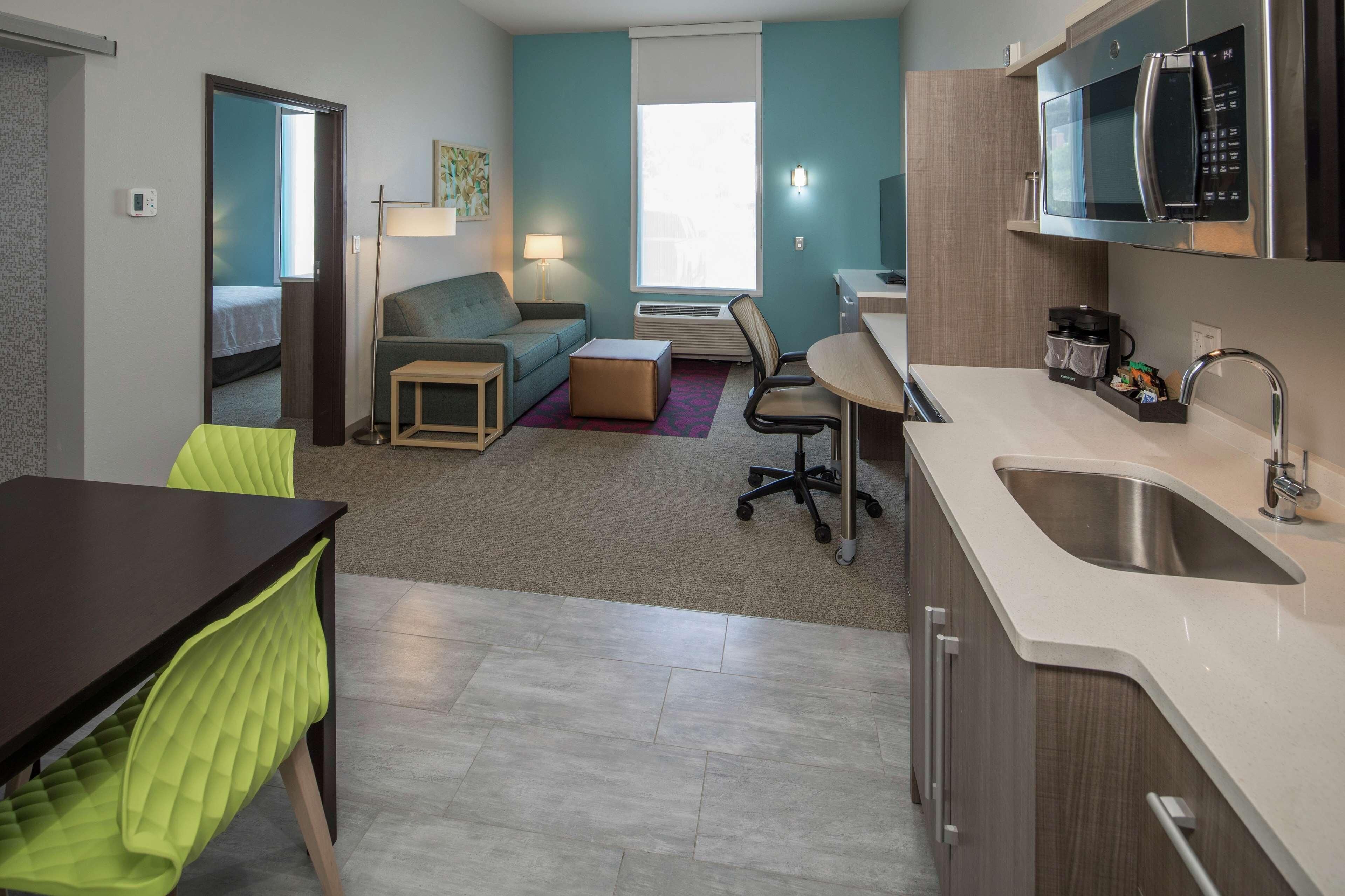 A compact hotel room with a kitchenette, a dining area, a sofa, and a small table.