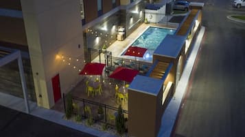 An outdoor pool area with umbrellas and chairs, surrounded by a fence and a building.