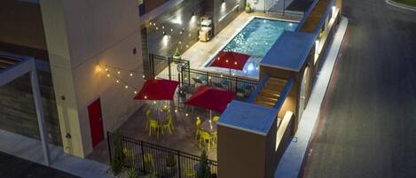 An outdoor pool area with umbrellas and chairs, surrounded by a fence and a building.