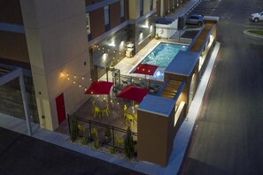 An outdoor pool area with umbrellas and chairs, surrounded by a fence and a building. - Home2 Suites by Hilton Owasso (Owasso)