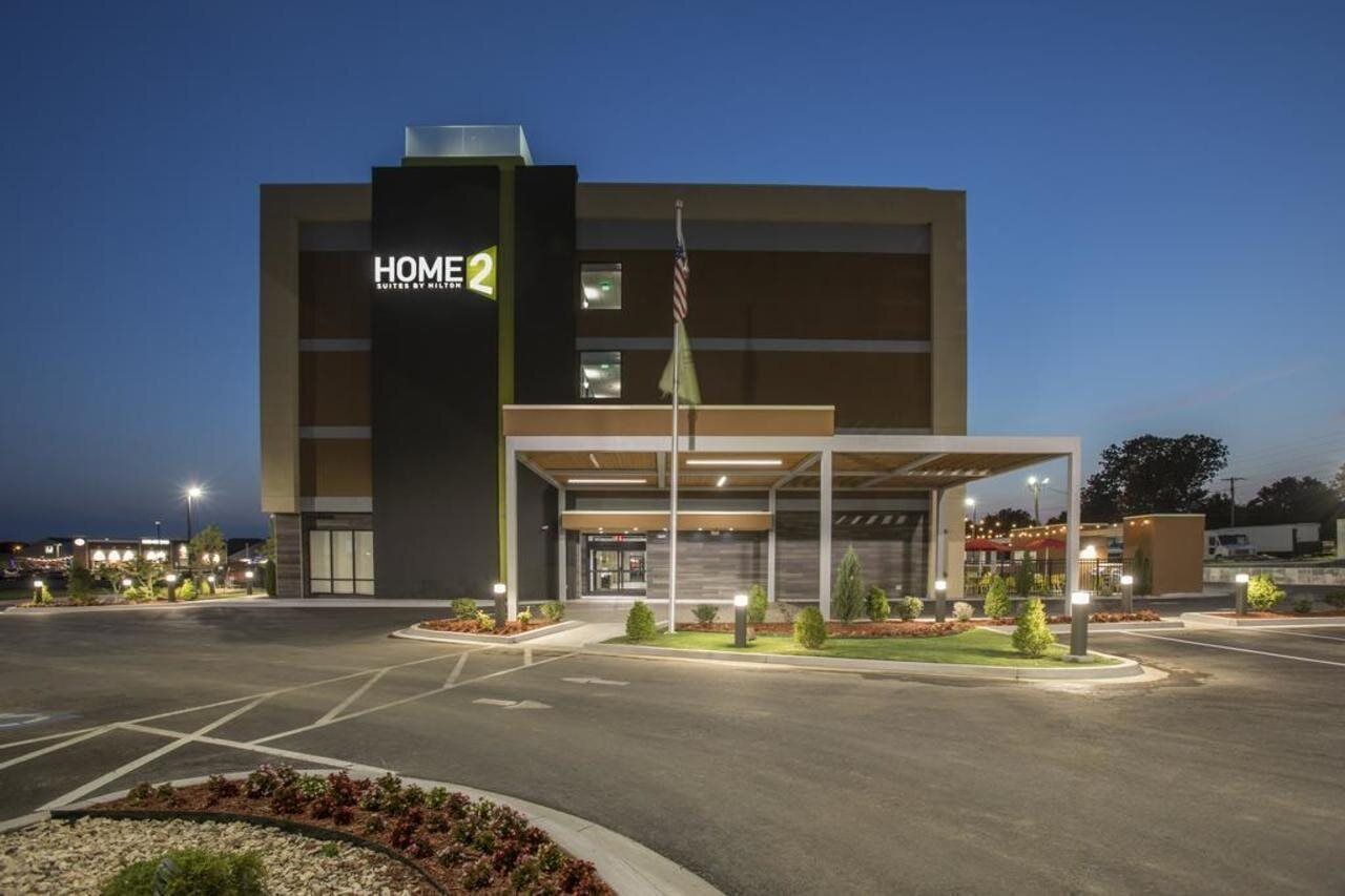 A modern hotel with a covered entrance, a flag, and a well-lit parking area.