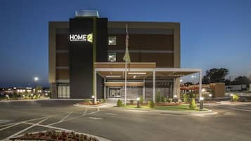 A modern hotel with a covered entrance, a flag, and a well-lit parking area.
