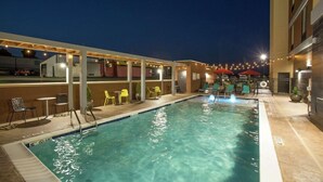 Un espace piscine avec des chaises et des tables, une piscine, et un bâtiment en arrière-plan.