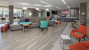Un espace de détente moderne avec un canapé, des fauteuils et des tables. On aperçoit un comptoir d'accueil avec un bureau et des étagères en arrière-plan.