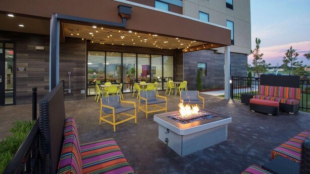 Un espace extérieur aménagé en terrasse, avec un foyer, des chaises jaunes et des assises aux couleurs vives.
