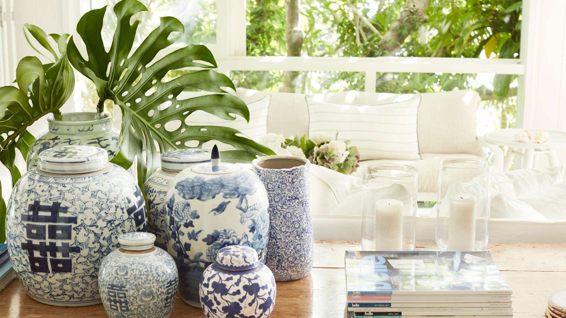 Une pièce dotée d’une grande fenêtre, de meubles blancs et de divers objets décoratifs, notamment des vases en céramique bleue et blanche et une plante en pot.