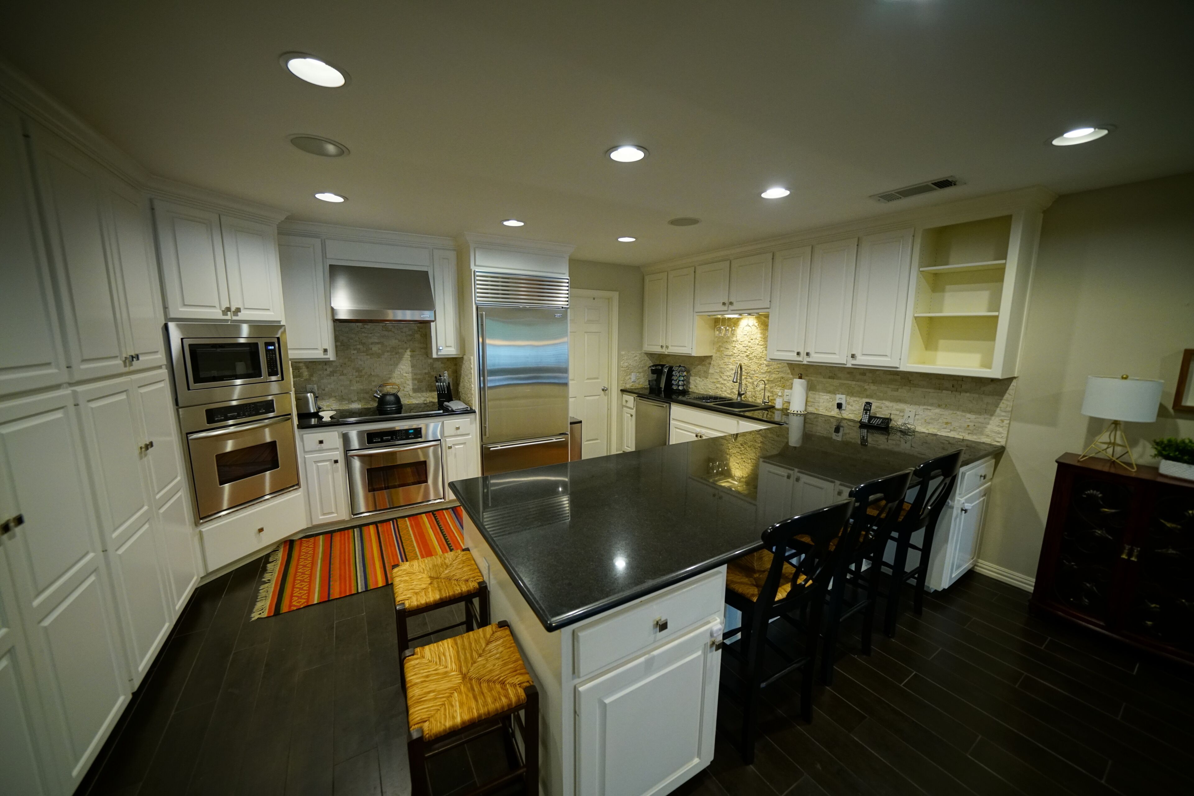 A modern kitchen with white cabinetry, stainless steel appliances, and a central island with bar stools.
