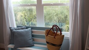 Un banco con una cesta tejida y un cojín junto a una ventana con vistas al verdor.