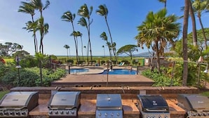 A pool area with multiple grills and palm trees. - Amazing Oceanview Beachfront Getaway Close to Everything! (Kihei)