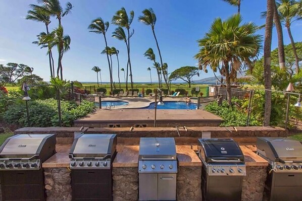 A pool area with multiple grills and palm trees. - Amazing Oceanview Beachfront Getaway Close to Everything! (Kihei)