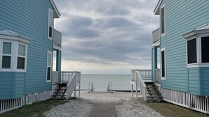 Um caminho leva a uma praia, com duas casas azul-claras de cada lado.
