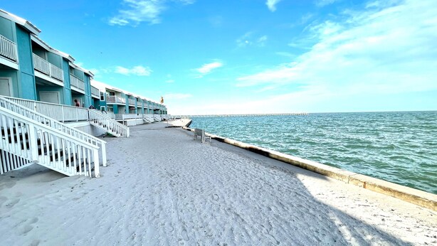 Um hotel à beira-mar com um calçadão de areia, grades brancas e vista para o oceano.