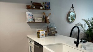 Cozinha moderna com armários brancos, lava-louças de aço inoxidável e bancada de mármore.