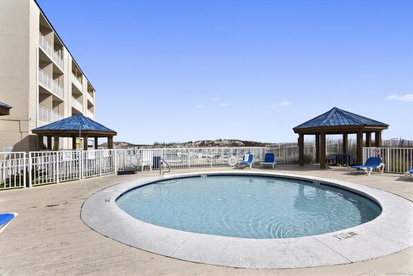 A swimming pool with a surrounding deck, two gazebos, and a building with balconies.