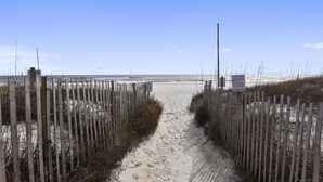 Un sentier de plage sablonneux, bordé de clôtures en bois et agrémenté d’un panneau.