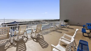Un balcon avec des chaises en plastique blanches, une piscine et une vue sur la plage et l’océan.