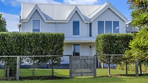 A two-story house with a symmetrical facade, a front porch, and a fenced yard with neatly trimmed hedges. - A Family home made for beach holidays & sunshine (PORT FAIRY)