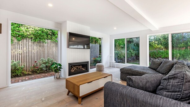 A modern living room with a fireplace, large windows, and a view of the garden. - A Family home made for beach holidays & sunshine (PORT FAIRY)