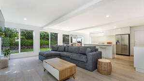 A modern living room with a grey sectional sofa, a wooden coffee table, and a wicker side table. - A Family home made for beach holidays & sunshine (PORT FAIRY)