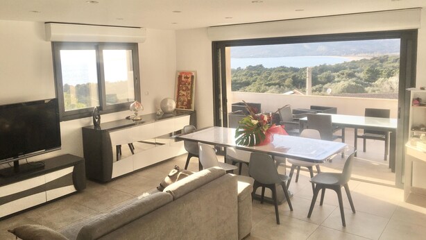 A modern living room with a sofa, dining table, and chairs, a TV, and a large window with a view of a mountainous landscape.