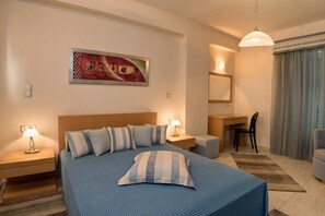 A hotel room with a large bed, a desk, a chair, a lamp, and a painting on the wall.