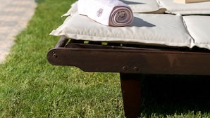 Een ligbed met een opgerolde handdoek en een boek, een pad, en lounge stoelen op de achtergrond.