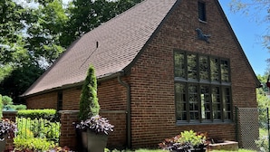 A brick building with a steeply pitched roof, large windows, and a small chimney.