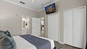 A bedroom with a bed, a TV, and a view of the kitchen.