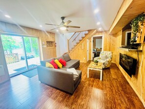 A spacious living area with a grey sofa, a coffee table, a television, and a staircase leading to another level. - Chalet Le Caribou au bord de l'eau et spa, kayaks, pedalo (Chertsey)